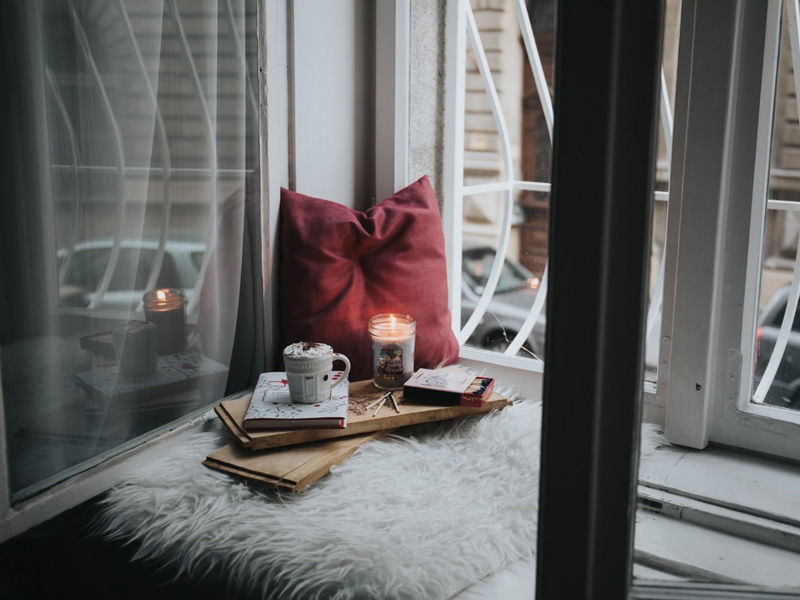 Image of burgandy pillow in a window nook with candle and books